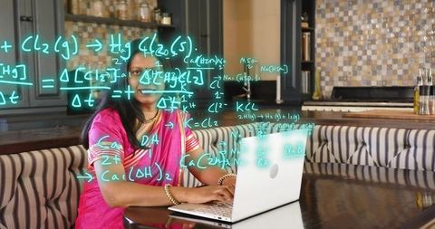 Mature indian woman in pink sari typing on laptop with chemistry and math equations