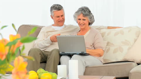 Smiling Mature Couple Using Laptop on Sofa Together