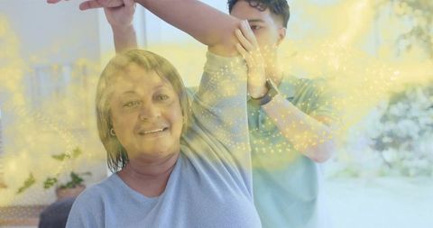 Caregiver assisting senior woman raising arm during home rehabilitation with smartwatch