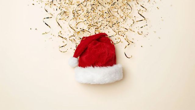Plush santa hat surrounded by gold confetti and curled ribbons on cream backdrop