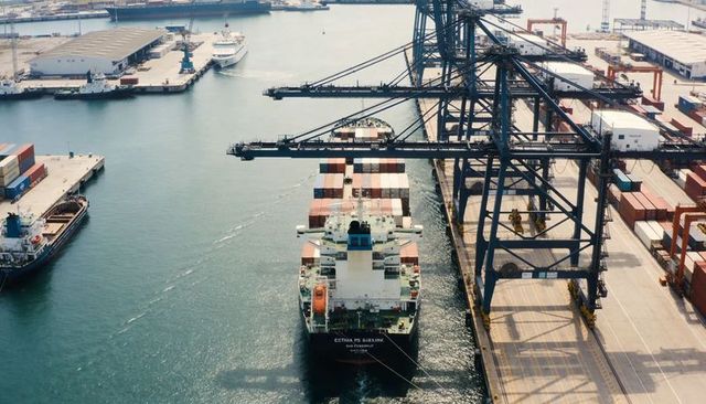 Container ship mooring under gantry cranes at container terminal, aerial port logistics