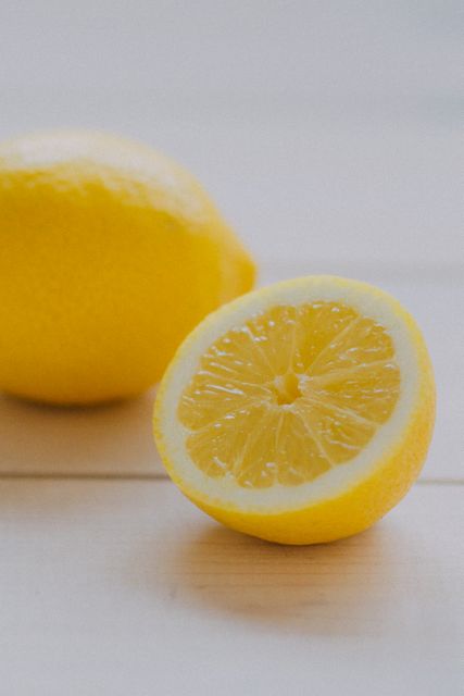 Close-up of a fresh lemon cut in half next to a whole lemon on a light wooden surface. Perfect for culinary ingredients, healthy eating, or vitamin C promotions. Ideal for food blogs, recipe sites, or health and wellness content.