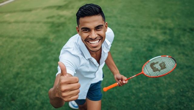 Energetic male athlete with thumbs up on outdoor badminton court