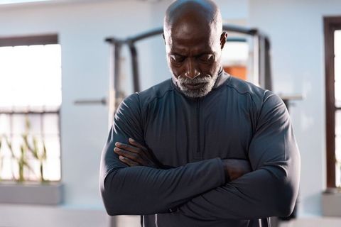 Senior african american man standing arms crossed in gym, contemplating strength and focus