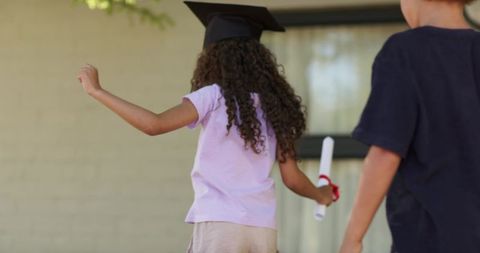 Sunlit backyard preschool graduation kids walking holding diploma and mortarboard