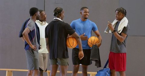 African american teammates laughing and chatting after pickup game holding basketballs