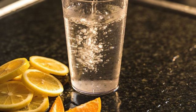 Pouring sparkling water into clear glass with lemon and orange slices on granite counter