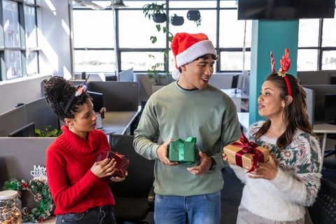 Diverse coworkers exchanging gifts in modern open-plan office holiday celebration