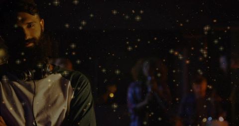 Bearded DJ Leaning and Adjusting Headphones in Moody Club with Raglan Shirt and Drum Kit