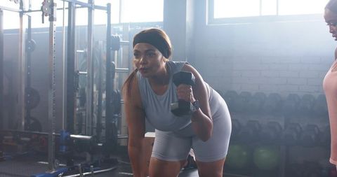 Diverse female training partners performing single-arm dumbbell row in industrial gym
