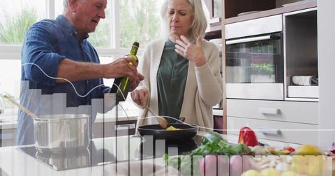 Mature couple cooking at kitchen island pouring olive oil stirring vegetables