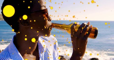 Black woman drinking from bottle by sunlit ocean with golden bokeh and seaside vibes