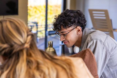 Young asian man leaning and smiling during casual conversation in sunlit lounge patio