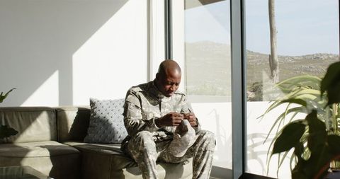 Soldier Reflecting While Holding Baby Clothes in Sunlit Room