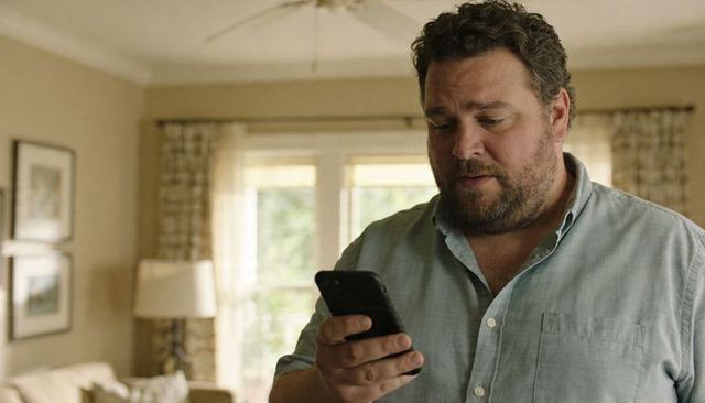 Bearded middle-aged man reading smartphone in cozy living room with natural light