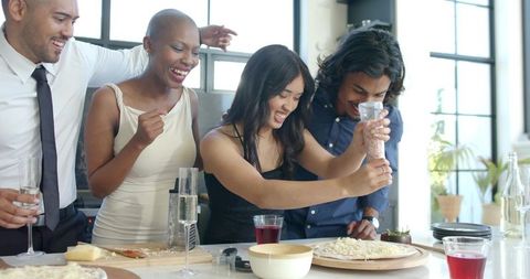 Laughing friends seasoning homemade pizza in bright modern kitchen