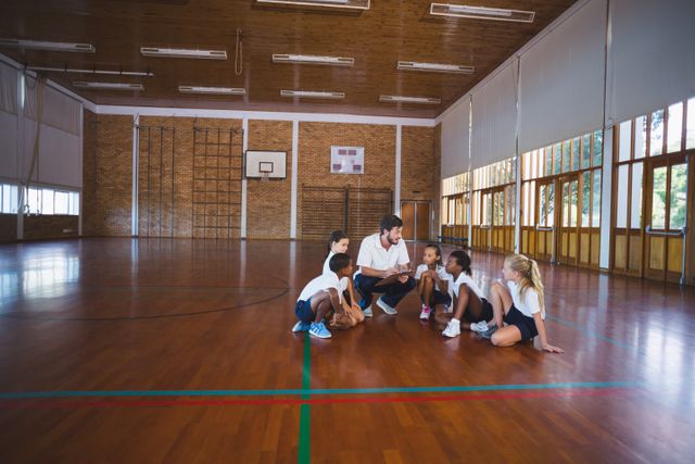 Sports teacher having discussion with his students in basketball court at school gym