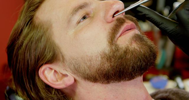 Caucasian man getting a precise beard trim at a barbershop. Expert barber provides grooming services, enhancing the man's facial hair style.