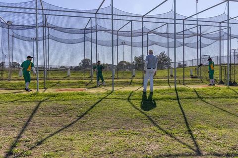 Coach calling batting drill in outdoor baseball cage during practice