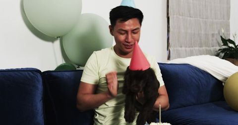 Man celebrating birthday with puppy and balloons on sofa