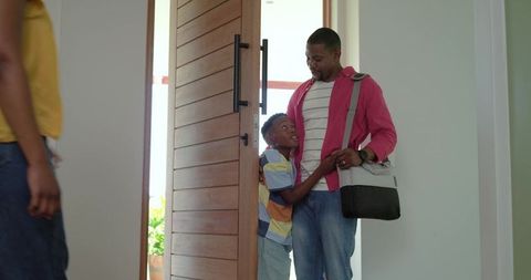 African american father saying goodbye to son at wooden front door carrying shoulder bag