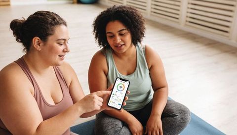 Two women checking fitness app on smartphone during at-home workout