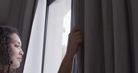 African american woman pulling grey curtain at window, soft morning light, calm profile
