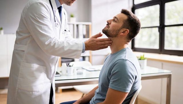 Physician examining male patient neck for thyroid and lymph nodes in bright clinic office