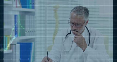 Contemplative senior doctor writing patient notes at desk with stethoscope and spine charts