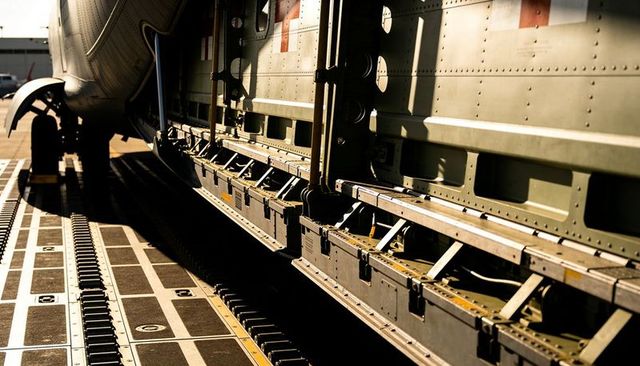 Sunlit cargo hold interior riveted panels, pallet rails and roller tracks at airport apron