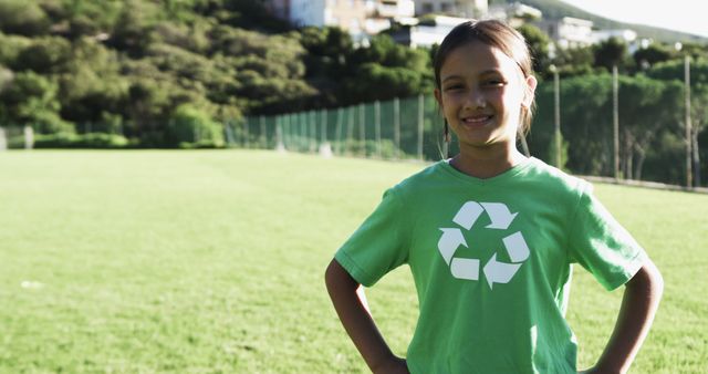 Young girl smiling while wearing a green recycling t-shirt outdoors. Promoting environmental awareness and sustainability. Ideal for use in content related to eco-friendly initiatives, youth activism, educational programs, conservation efforts, and community involvement in protecting the environment.
