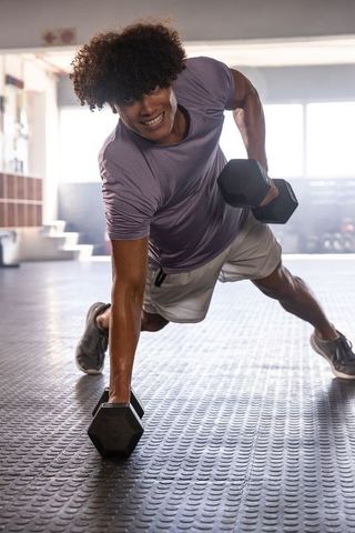 African American man performing renegade row plank with hex dumbbells on rubber gym flooring
