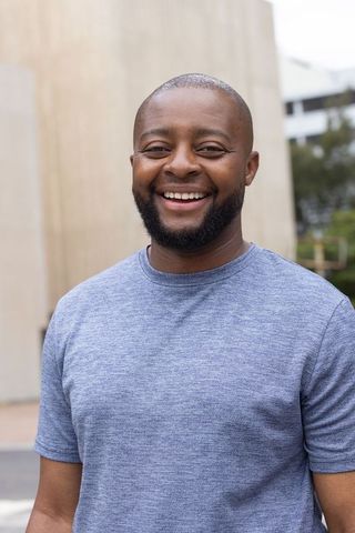 Smiling african man standing in urban plaza wearing casual blue t-shirt portrait