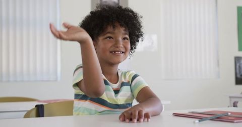 African American boy smiling and raising hand in classroom, sitting at school desk