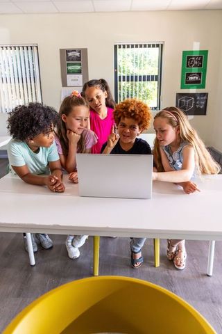 Multiracial elementary children collaborating around laptop, learning math and teamwork