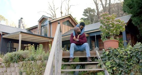 African american father and son sharing joyful hug on wooden porch steps of modern home