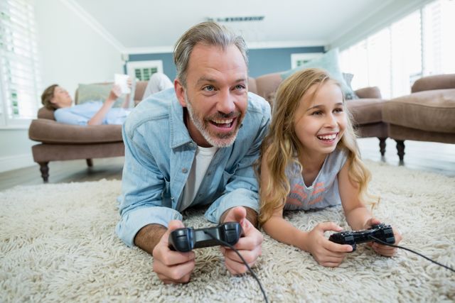 Father and daughter enjoying quality time playing video games together on the floor of their living room. Ideal for use in family-oriented content, advertisements for gaming consoles, or articles about parent-child bonding and leisure activities.