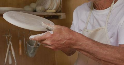Senior craftsman expertly shaping pottery dish in studio workshop