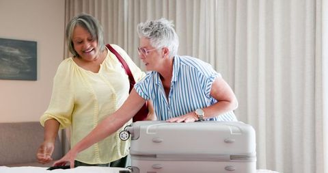 Senior lesbian couple packing for summer vacation with joyful interaction