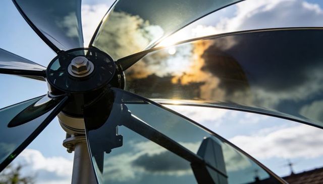 Glossy translucent rotor blades reflecting sun and clouds over rooftop turbine hub, close-up