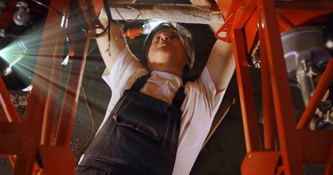 Mechanic working under vehicle on red lift repairing wiring and plumbing in industrial garage