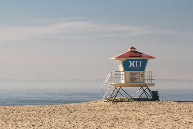 Lonely lifeguard tower standing on quiet sandy beach, surrounded by the calm sea under a clear sky. Ideal for use in travel promotions, coastal safety materials, summer getaway advertisements, or relaxing scene representations.