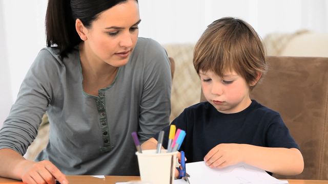 Mother engaging with her young son while he draws, showcasing a bonding moment through creative expression. Ideal for depicting family life, educational activities, or promoting positive parenting at home. Demonstrates creativity's role in childhood development and parental involvement.