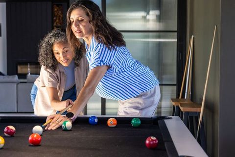 Multiracial women playing pool at home, coaching shot and enjoying game night