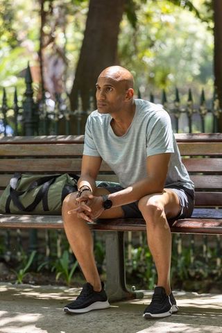 Contemplative man sitting on park bench with duffel bag under dappled sunlight