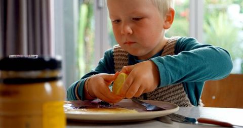 Boy Squeezing Lemon on Pancake at Dining Table