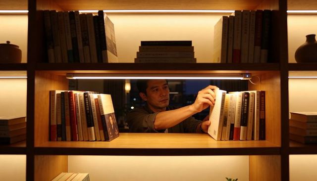 Man reaching for book on warmly lit wooden bookshelf with led lighting in library alcove