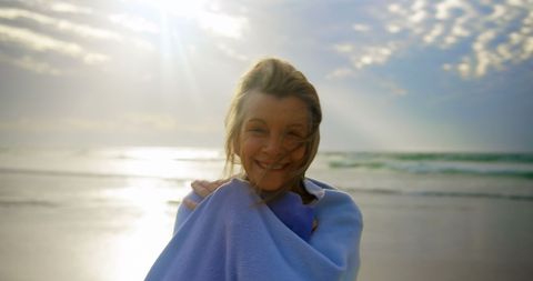 Senior woman enjoying sunny day at the beach wrapped in shawl