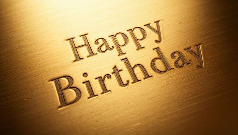 Engraved happy birthday on brushed gold metal plaque with warm luxury texture
