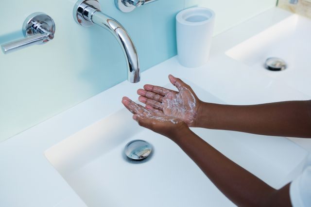 Child washing hands with soap in a modern bathroom sink. Promotes hygiene and cleanliness. Useful for health and sanitation campaigns, educational materials on handwashing, and advertisements for bathroom fixtures or soap products.